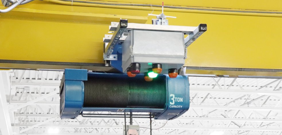 A 3-ton capacity electric wire rope hoist with an integrated control unit mounted on an overhead crane bridge in a manufacturing facility.